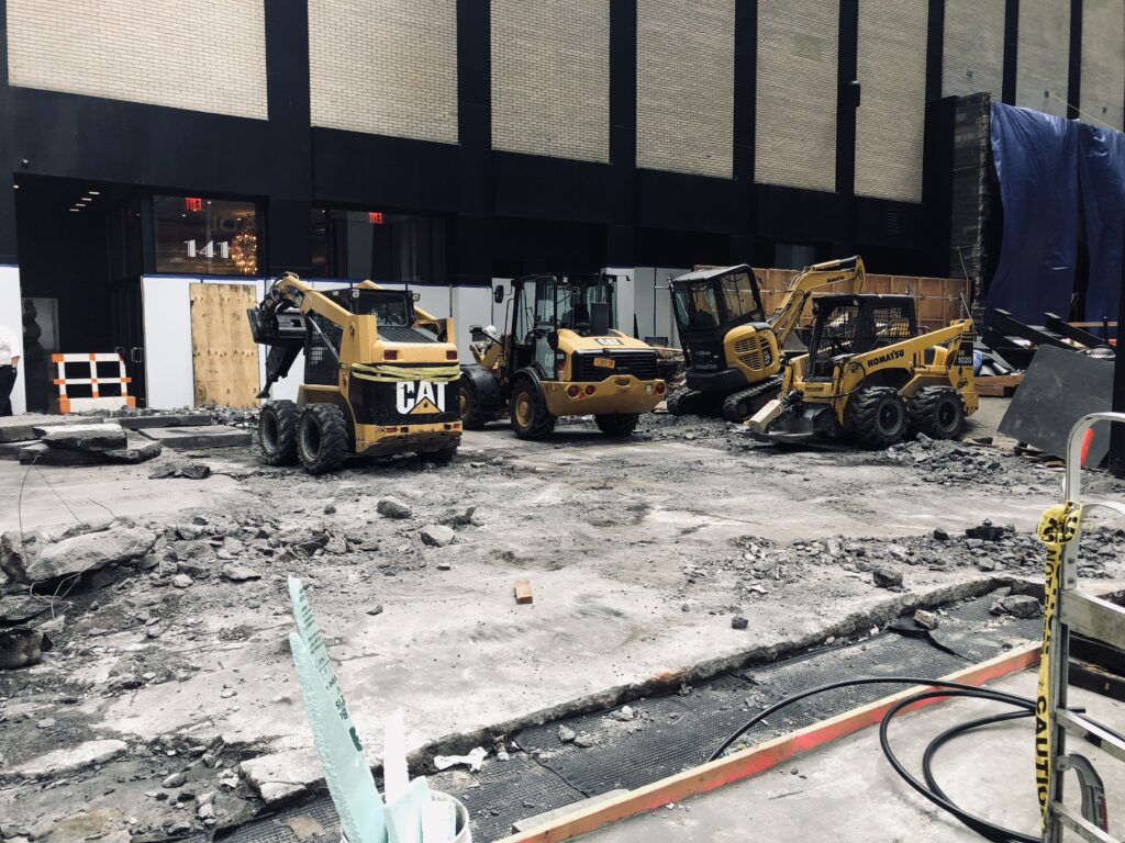 A Construction Site With Broken Concrete and Three Yellow Construction Vehicles.