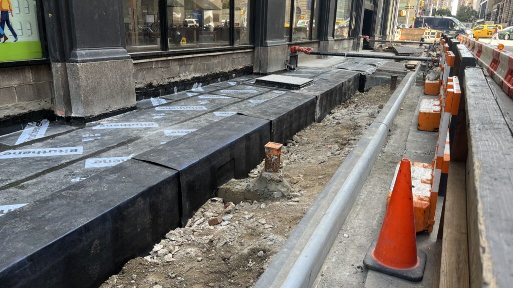 A Street Under Construction With a Dug-up Sidewalk Covered by Black Waterproofing Sheets.